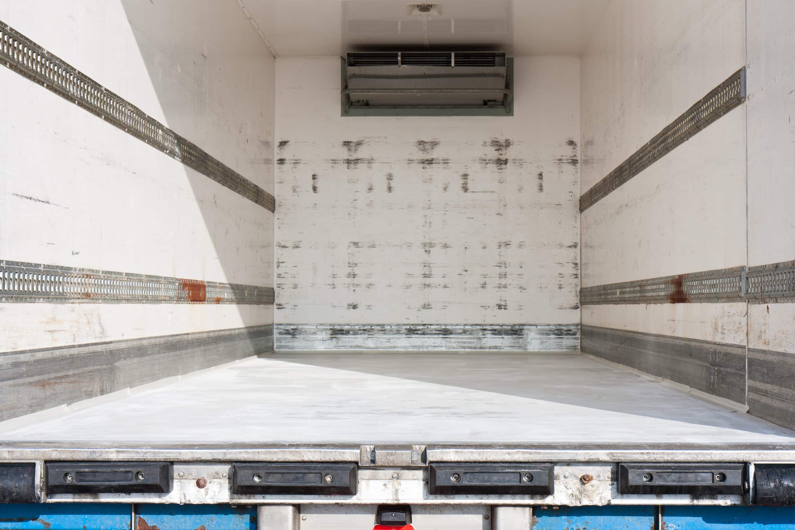 An empty semi-trailer with white walls and four E-track rails, two on each side wall, shows signs of rust and wear.