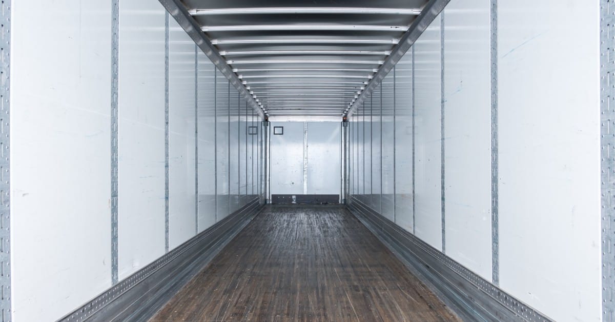 4 Tips for Proper Installation of Cargo Load Bars The inside of an empty semi-trailer with white walls, vertical metal lines, and scuffed hardwood flooring.