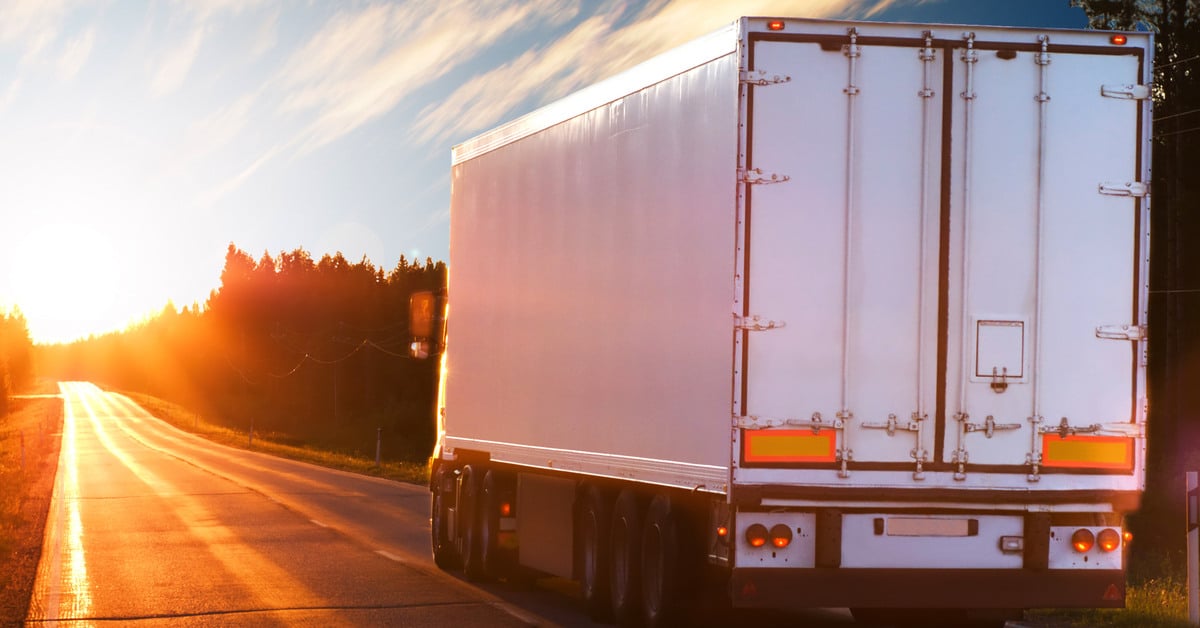 Logistick-361423-white-freight-truck-image1 A white freight truck drives down a highway surrounded by trees. The back of the truck is visible.